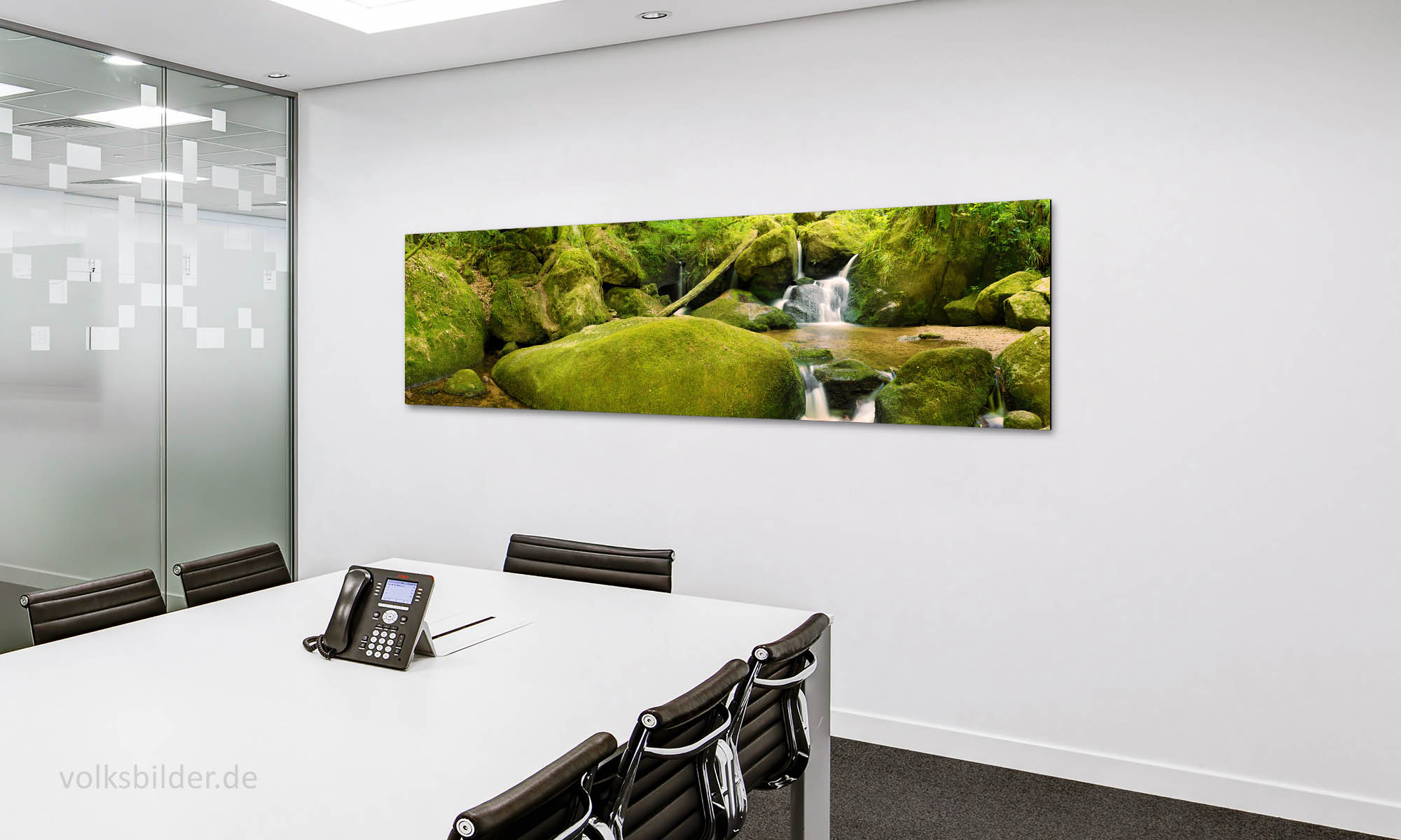 Foto von einem Besprechungsraum in einem Büro. An der Wand im Hintergrund hängt ein breites Panoramabild mit einem Foto von einem Waldbach.  