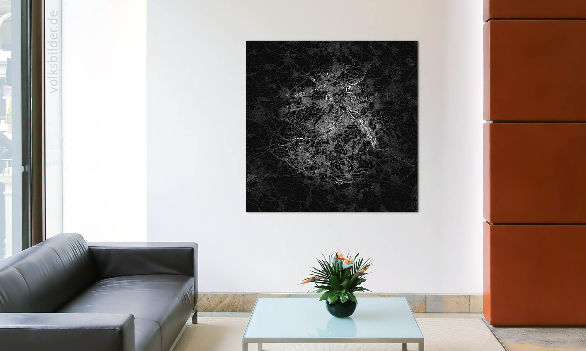 Foto eines Warteraumes oder Foyers einer Firma. Neben einer schwarzen Couch steht ein Couchtisch. An der Wand im Hintergrund hängt ein quadratisches Wandbild. Dieses zeigt eine schwarz-weiße Karte vom Stadtgebiet von Stuttgart und der näheren Umgebung.