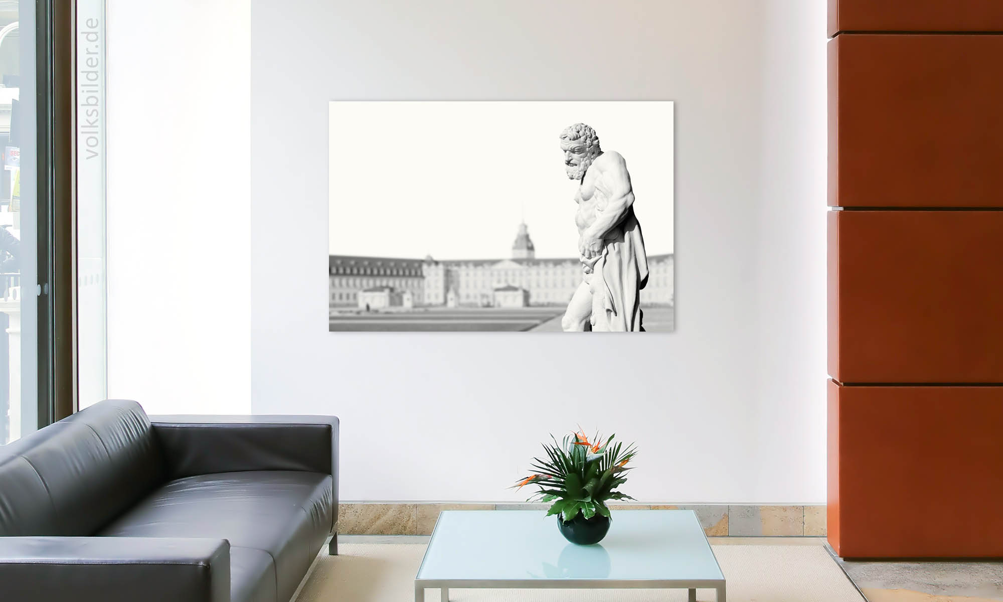 Das Foto zeigt ein Foyer eines Büros. Links steht eine Couch, rechts davon ein Couchtisch. An der Wand im Hintergrund hängt ein Wandbild mit einem High-Key-Foto der Statue des Herkules auf dem Schlossplatz vor dem Schloss in Karlsruhe.